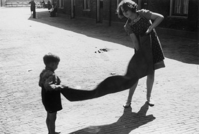 221134 Afbeelding van een jongetje die een vrouw helpt bij het uitkloppen van een kleed in de Hoogstraat te Utrecht.
